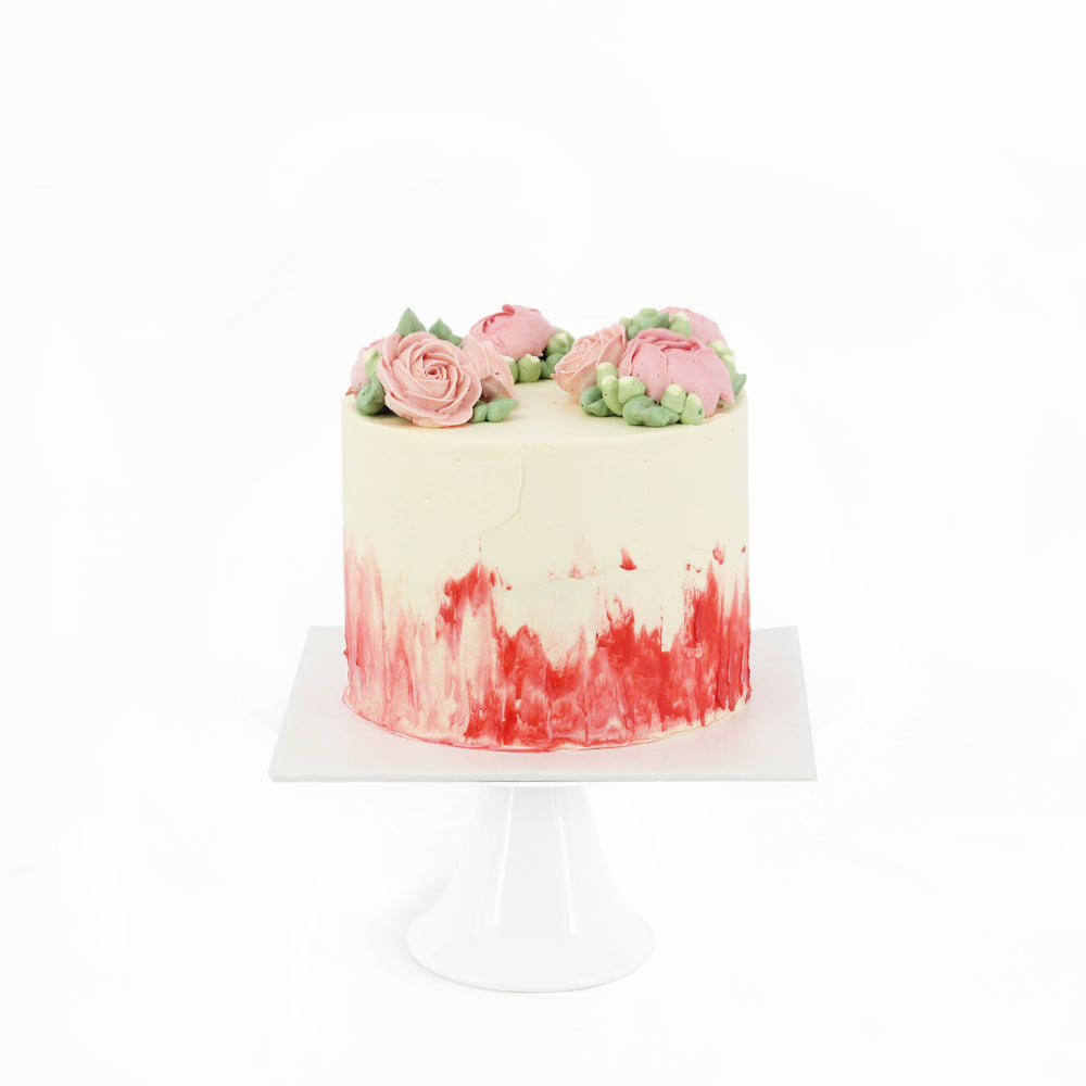 Cake frosted in red and white buttercream, adorned with hand piped pink roses