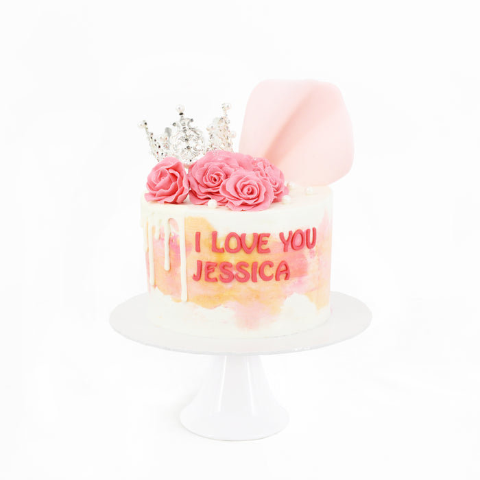 White buttercream frosted cake with pink and orange accents, topped with roses and a crown