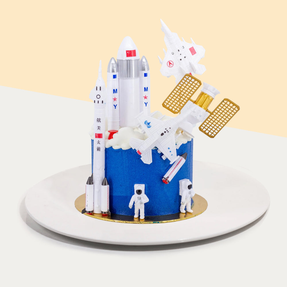 Blue space themed cake, with toy astronauts, rockets and satellite 