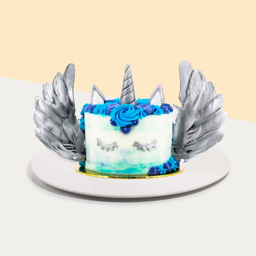 Unicorn cake with silver lashes, horn and ears, with silver wings and blue cream swirls