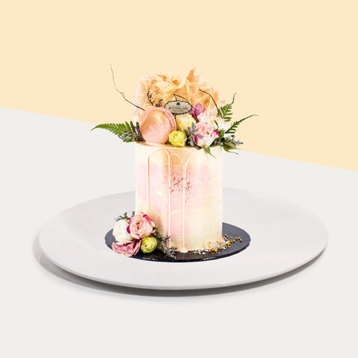 Butter cake decorated with pink and yellow buttercream, topped with macarons and fresh flowers