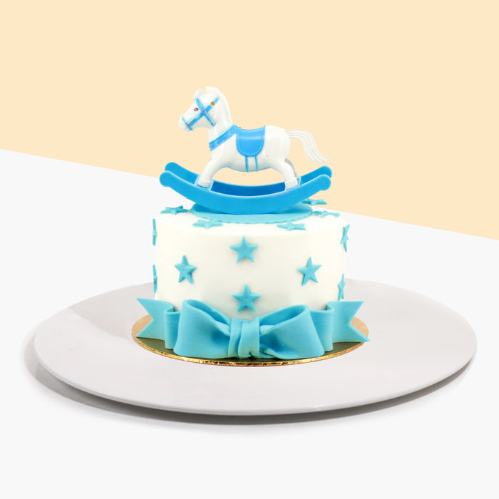 Butter cake cladded with white fondant, decorated with fondant stars and ribbon, and a rocking pony figurine