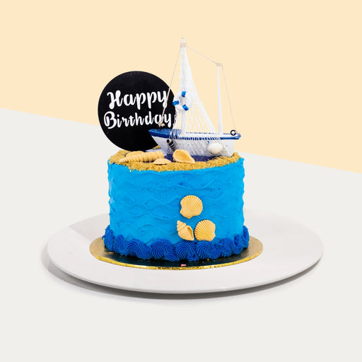 Butter cake frosted with blue wavy buttercream, decorated with seashells and a toy sail boat