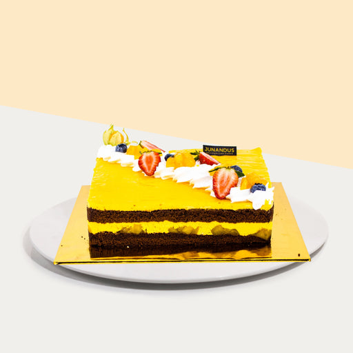 Chocolate cake with mango mousse and mango chunks, topped with fresh cream and fruits