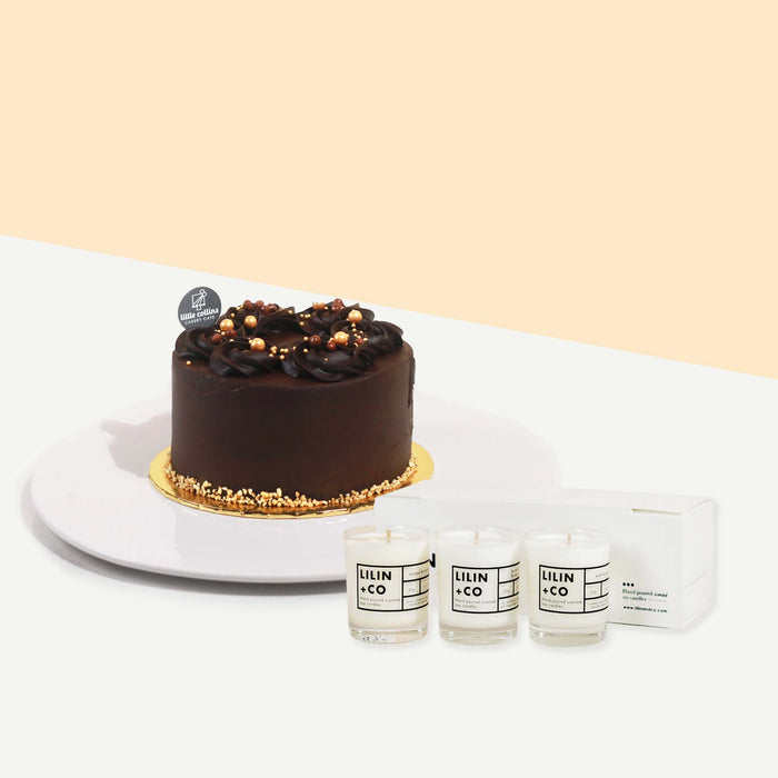Chocolate cake topped off with edible pearls, beside a bundle of scented candles