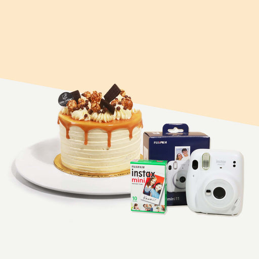 Cake coated with cream and caramel drizzle, garnished with chocolates and caramel popcorn with an Instax Camera with Instax film