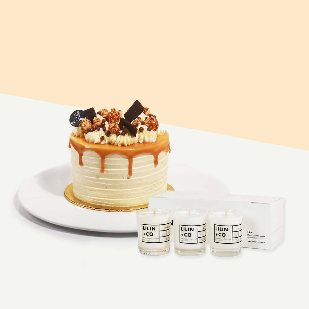 Cake coated with cream and caramel drizzle, garnished with chocolates and caramel popcorn with a bundle of scented candles of three
