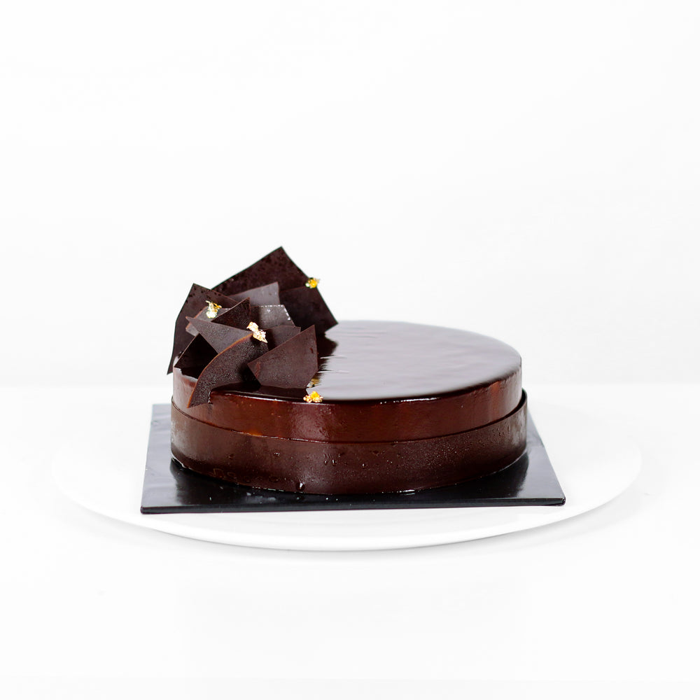 Shimmering dark chocolate cake, adorned with chocolate shards and edible gold