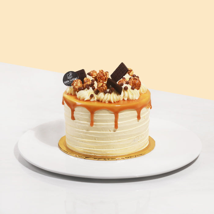 Cake coated with cream and caramel drizzle, garnished with chocolates and caramel popcorn