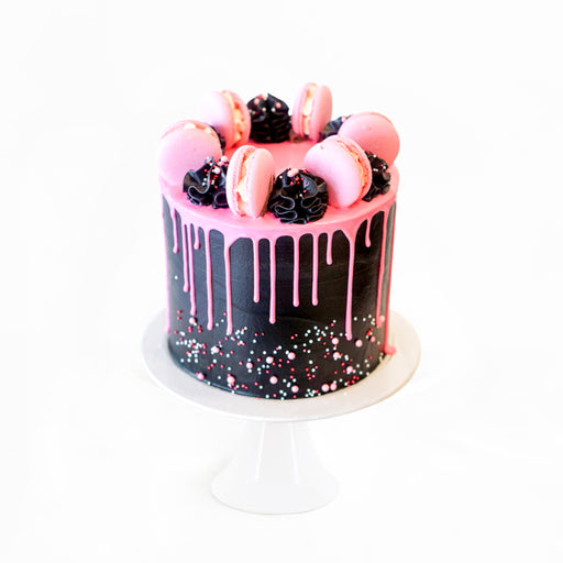 Black buttercream cake, topped with pink glaze, black cream swirls and pink macarons