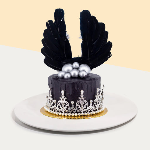 Black buttercream cake, decorated with a crown, silver spheres and black wings