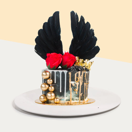 Black buttercream cake wit golden decorations, faux red roses, and black wings topper