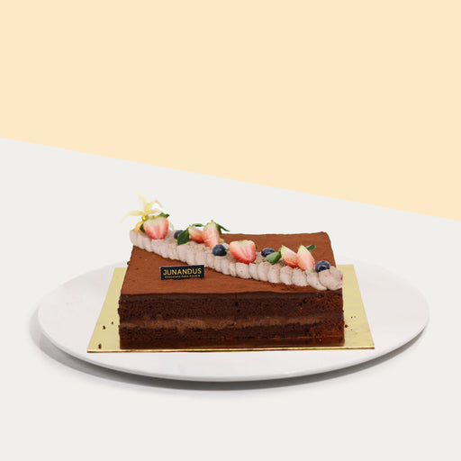Rectangular chocolate cake, coated with cocoa powder, garnished with cream and fresh fruits