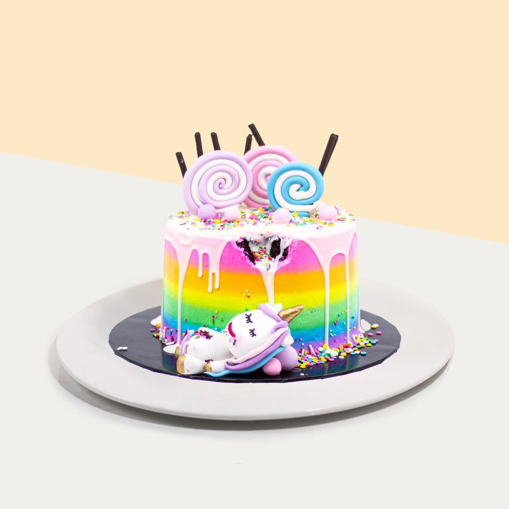 Rainbow themed cake with a unicorn taking a bite from the cake