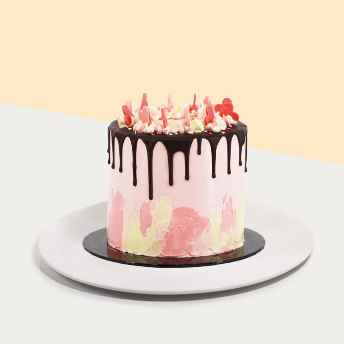Baby pink buttercream cake with abstract designs, chocolate glaze, and heart shaped sprinkles
