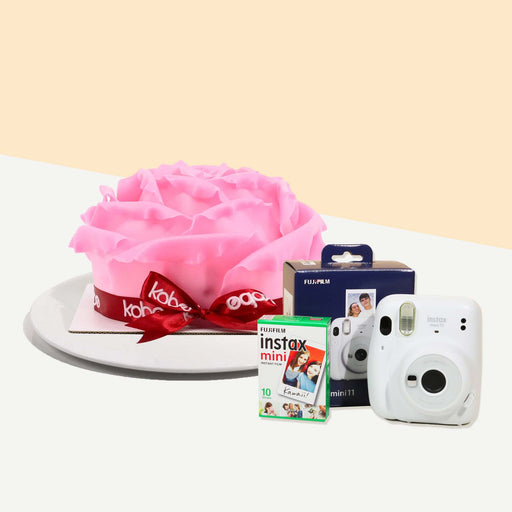 Cake decorated with pink chocolate fondant rose petals, wrapped with a ribbon with an Instax camera and film