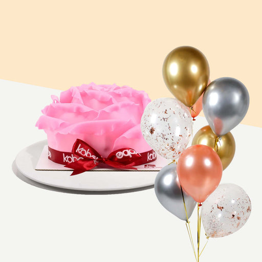 Cake decorated with pink chocolate fondant rose petals, wrapped with a ribbon with a bundle of balloons
