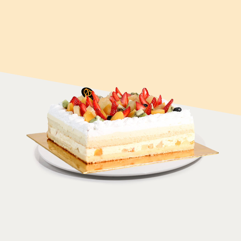 Rectangular vanilla sponge cake with mango and cream filling, topped with fresh cream and fruits
