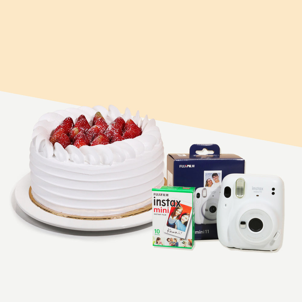 Cake coated with cream, topped with fresh strawberries with an Instax camera and film