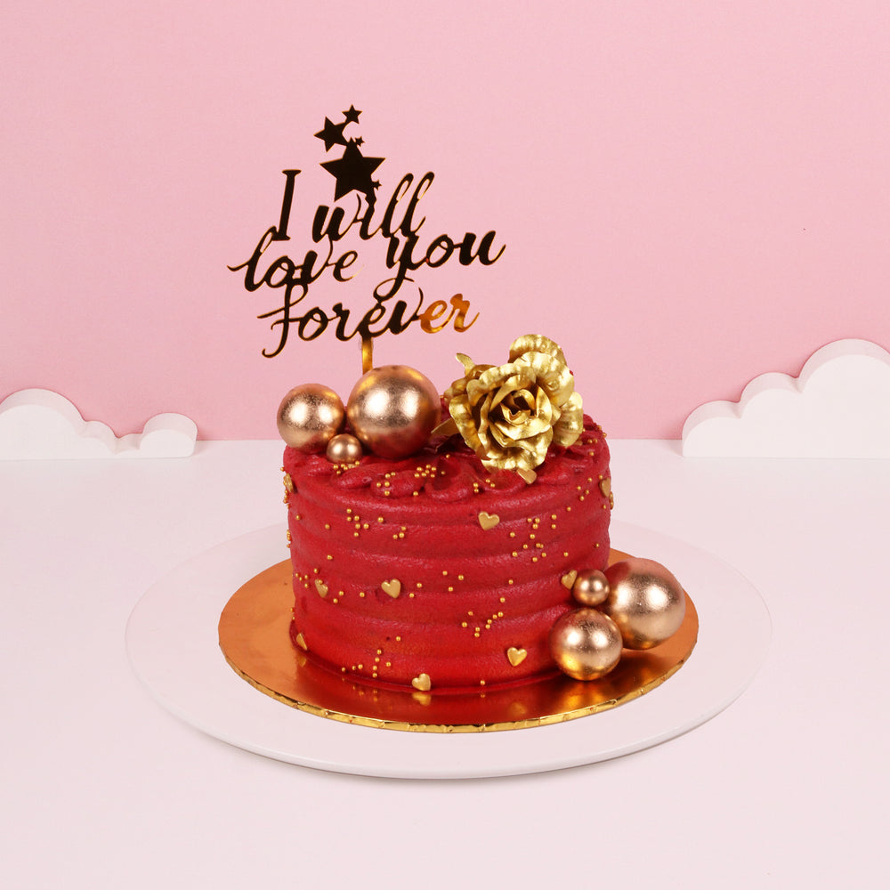 Red buttercream cake adorned with golden decorations, with a I Will Love You Forever cake topper