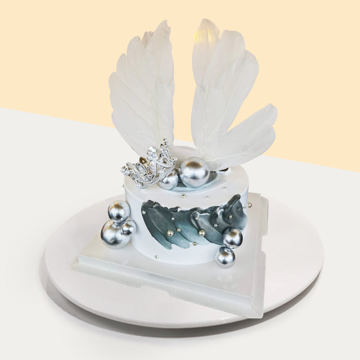 White cake decorated with grey paint swipes, topped with a crown and white feathers