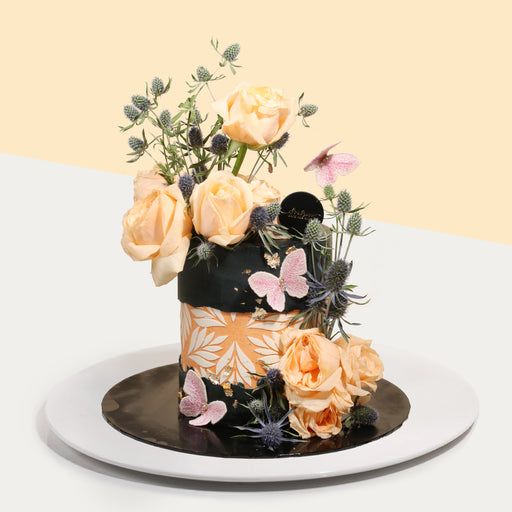 Black buttercream cake, with orange floral fault-line design, decorated with fresh flowers
