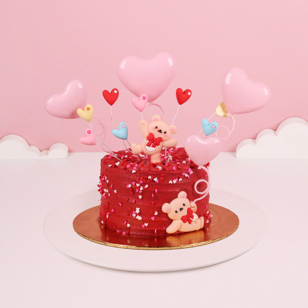Red butter cream cake topped with fondant bear figurine, and heart shaped sprinkles