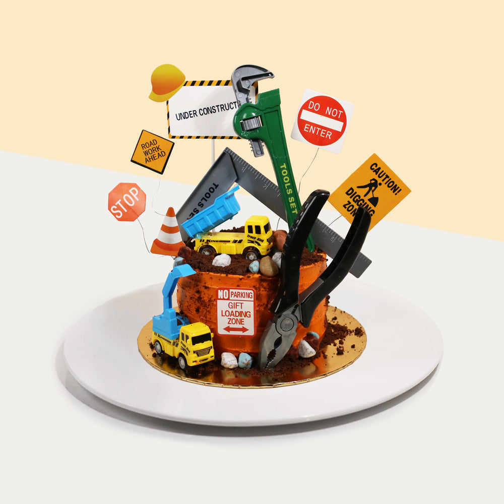 Construction themed cake with toy lorries, pliers, wrench and L-shaped ruler