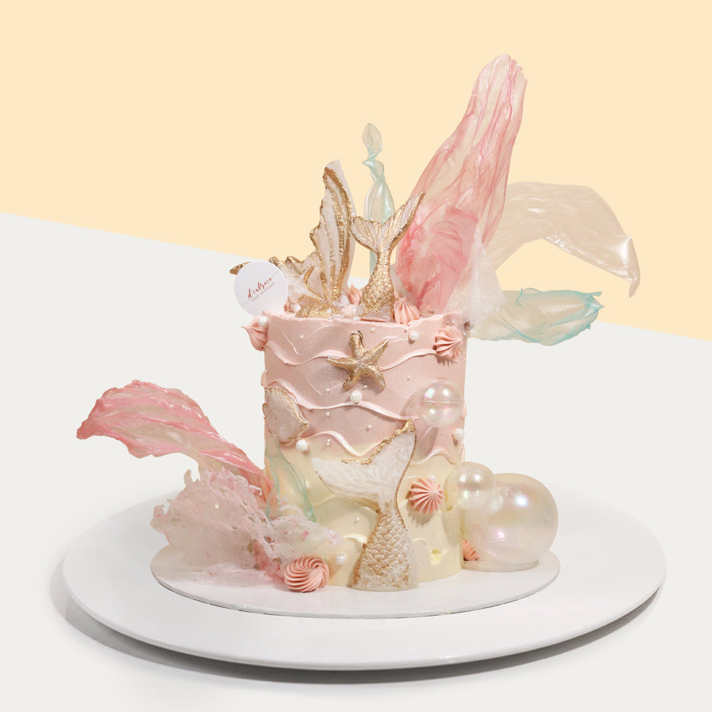 Butter cake with pink and white buttercream frosting, decorated with mermaid tails and rice paper sails