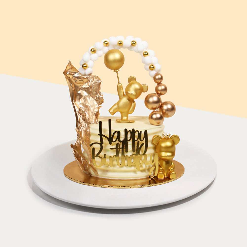Cake with golden decorations, including golden teddy bears holding balloons