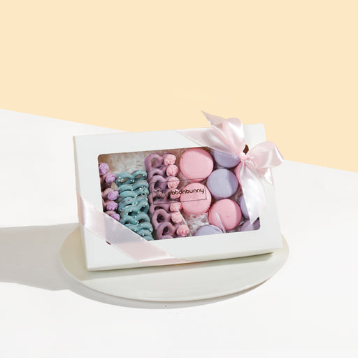 Mini pretzel and macarons of pink, purple and green, in a while box with ribbons
