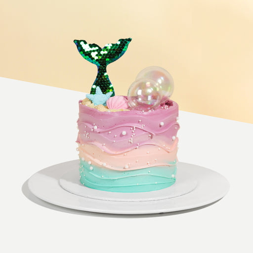 Cake coated with teal, pink and purple buttercream, with a dazzling mermaid tail on top