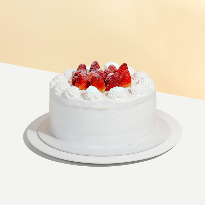 Vanilla sponge cake with signature cream cheese frosting, with fresh strawberries between the layers and on the cake