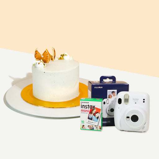 Small cake coated with fresh cream, garnished with dried orange slices and crushed pistachios with a set of Instax products