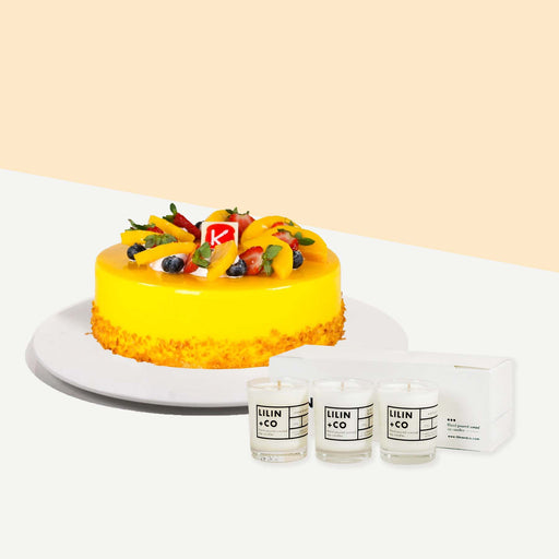 Yellow cake with mango fruit filling, topped with more mangoes, strawberries and blueberries with a set of Lilin+Co scented candles