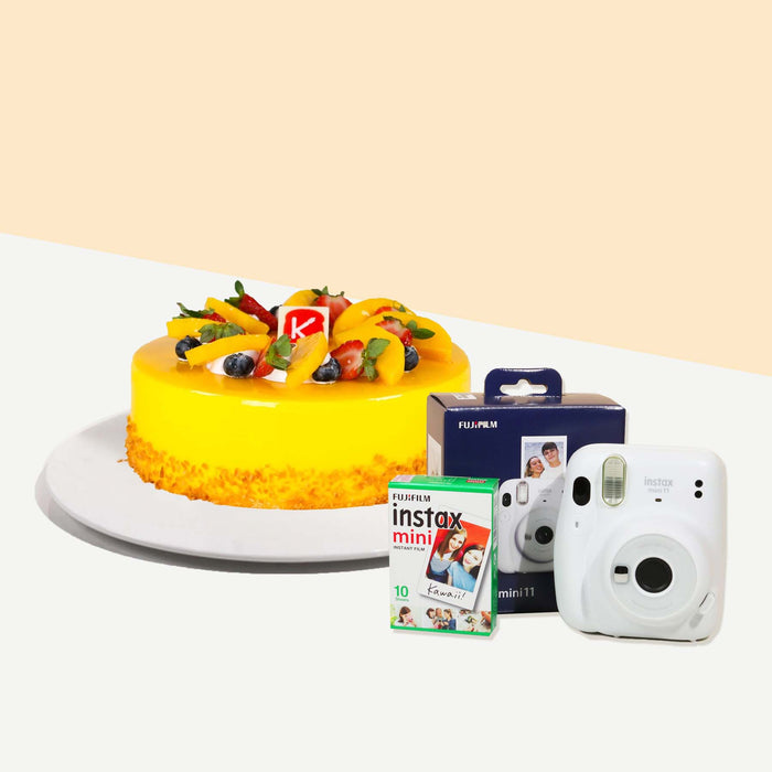 Yellow cake with mango fruit filling, topped with more mangoes, strawberries and blueberries with an Instax mini camera and film