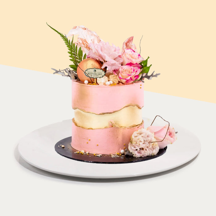 Pink and yellow buttercream cake with a golden fault-line, topped with fresh flowers and macaron