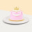 Pink princess cake with white buttercream drapes, topped with a golden crown topper