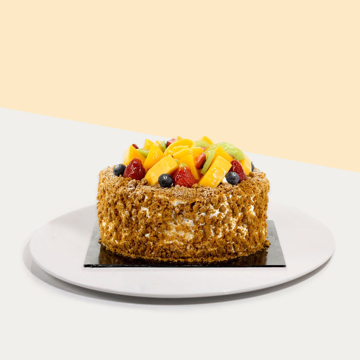 Cake covered with biscoff crumbs, topped with fresh mangoes, strawberries, kiwis and blueberries